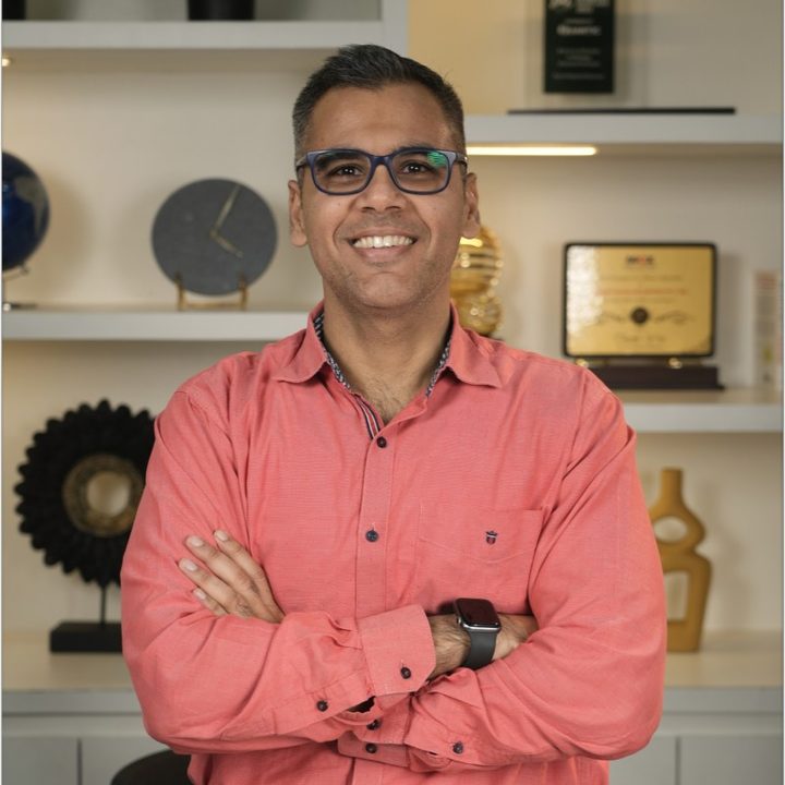 Faiyaz M Khairaz, smiling, arms crossed, in a coral shirt and blue glasses